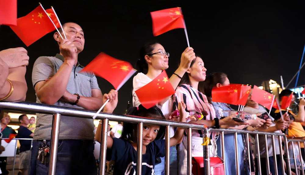 在“人民紅”快閃店門前，觀眾們舉著手中的五星紅旗觀看表演。